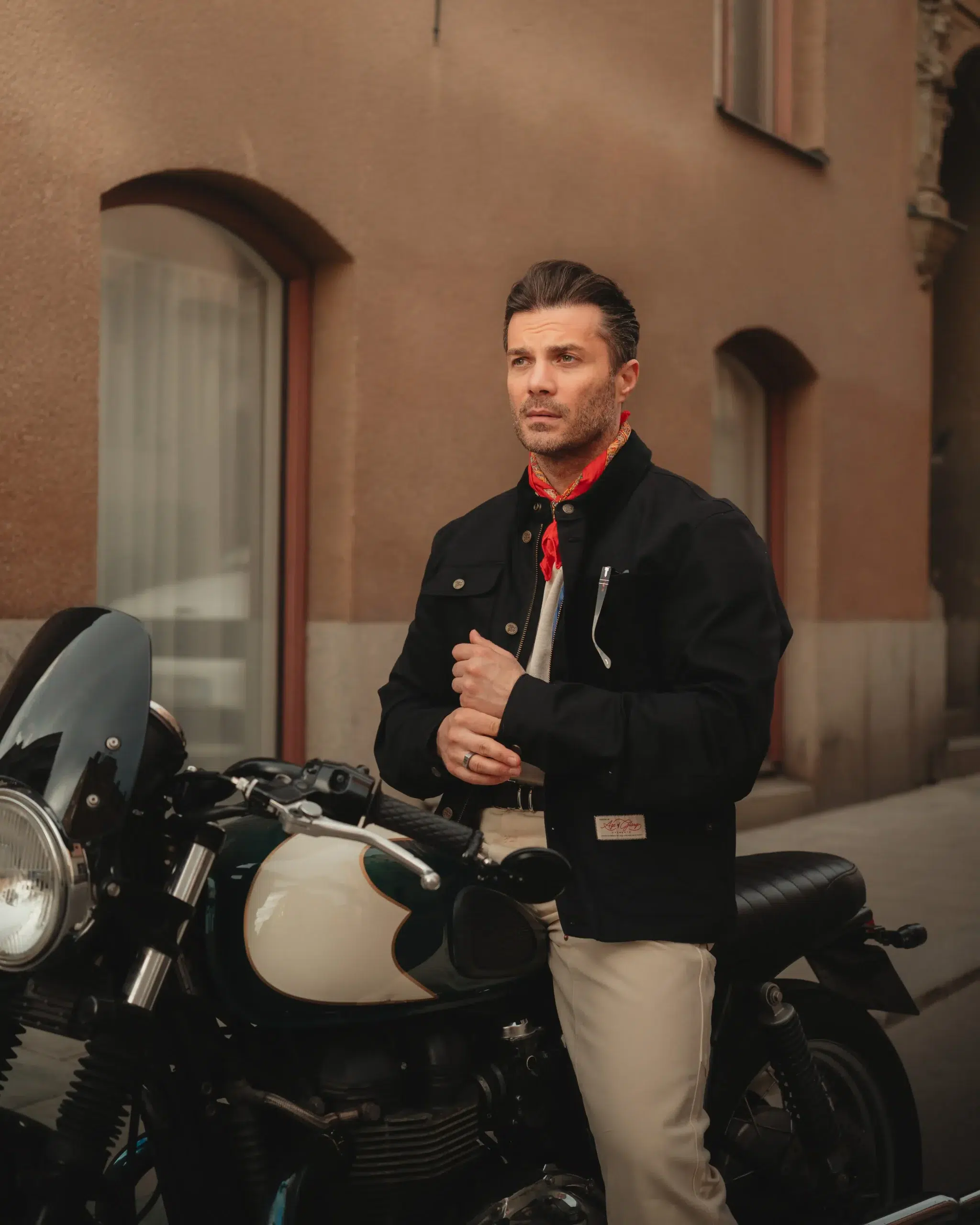 Man wearing a black jacket and red scarf beside a motorcycle